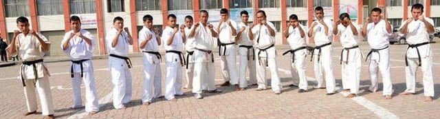 A line of black belts standing in formation in a stadium.