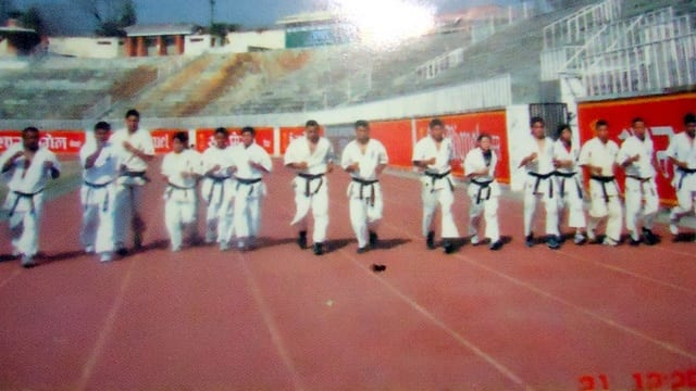 Karateka lined up in formation in a stadium before a red wall.